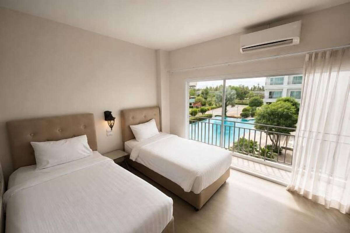 A hotel room with two beds, a balcony with a pool view, and an air conditioning unit.