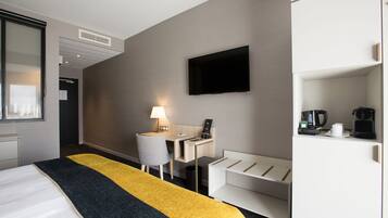 Une chambre d’hôtel équipée d’un lit, d’un bureau avec une lampe, d’une télévision, d’une machine à café et d’un mini-bar.