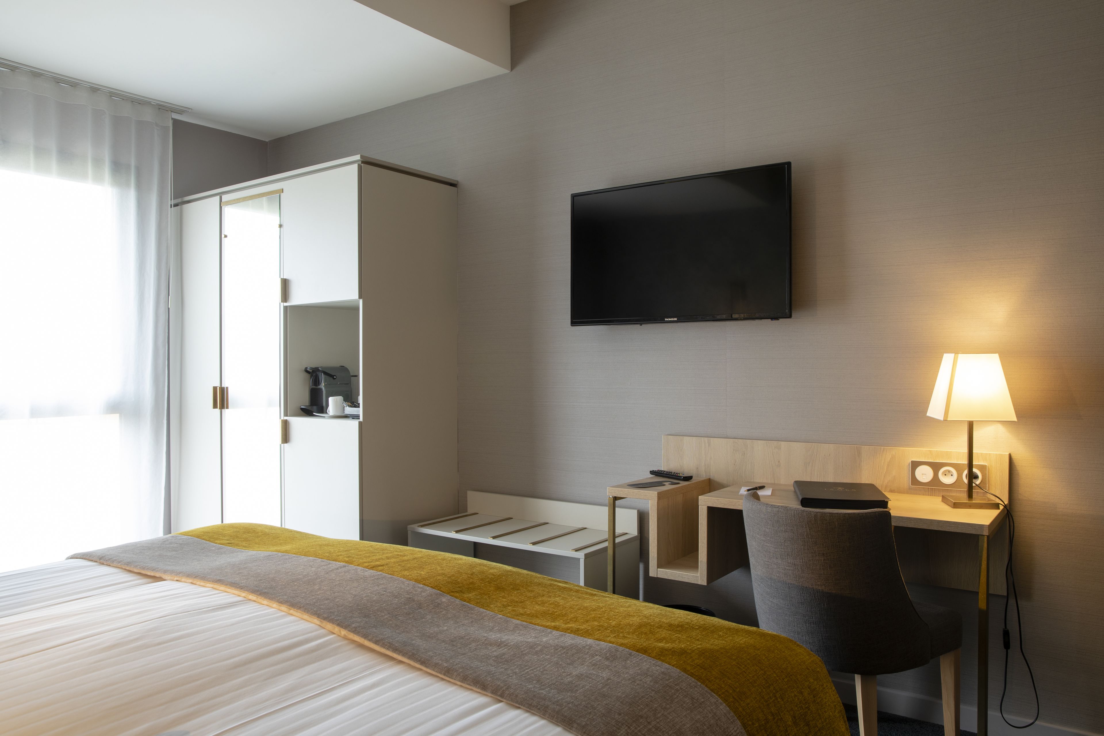 A hotel room with a bed, a desk, a chair, a TV, and a lamp.