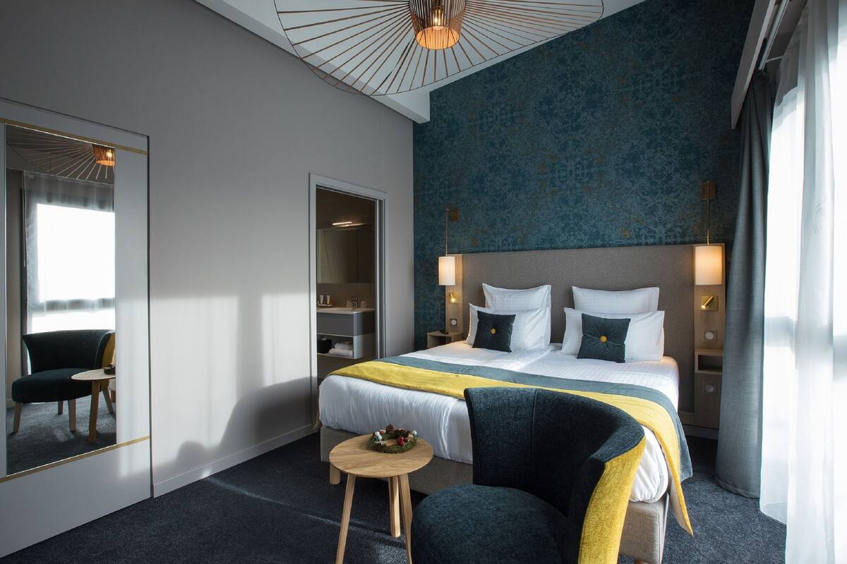 A hotel room with a large bed, a bedside table, a chair, a mirror, and a wardrobe.
