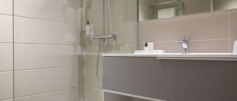 A modern bathroom with a glass shower enclosure, a large mirror, and a vanity with a towel rack.