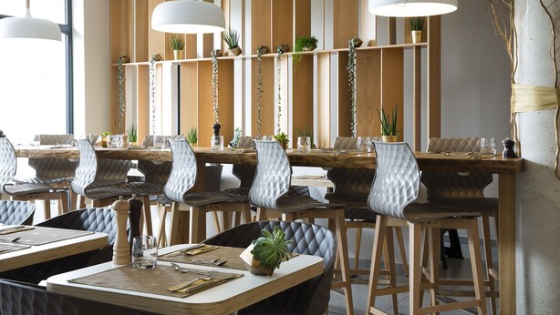 A modern dining area with wooden tables and chairs, pendant lighting, and plants on shelves. - James Boutique Hôtel (Colmar)