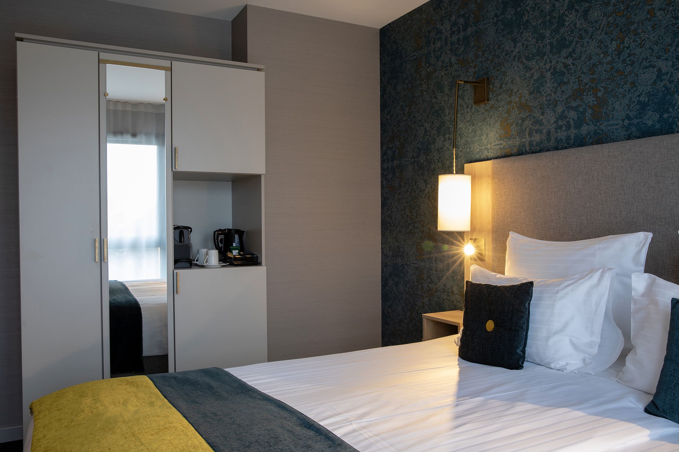 Une chambre d’hôtel comprenant un lit, une armoire, une table de chevet et une lampe fixée au mur.