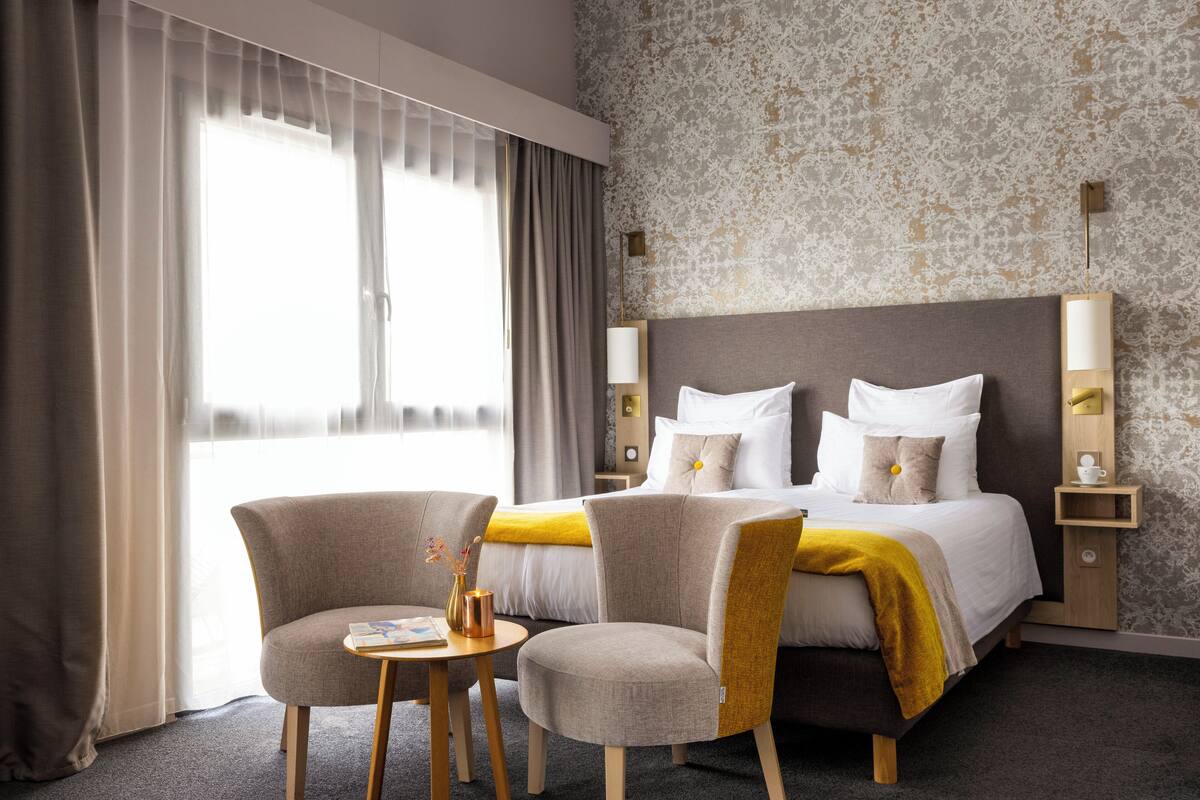 A hotel room with a bed, two armchairs, a small table, and a nightstand.
