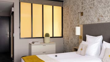 A hotel room with a bed, a nightstand, a lamp, and a window with curtains.