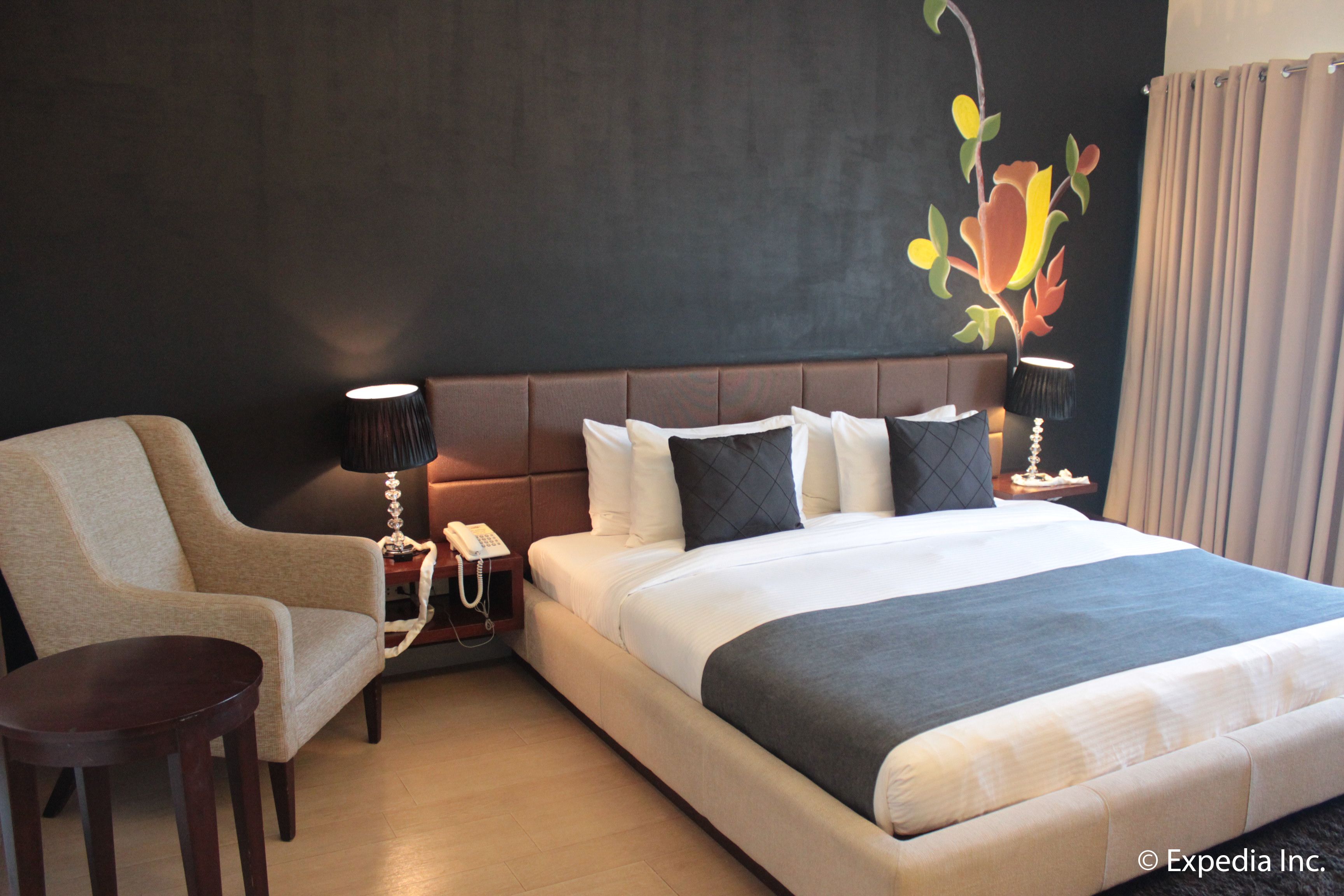 A hotel room with a large bed, a chair, a bedside table with a lamp, and a telephone.