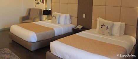 A hotel room with two beds, a chair, and a mirror.