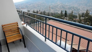 A balcony with a wooden bench, a metal railing, and a view of a cityscape with mountains in the distance. - La Posh Hotel (Kigali)
