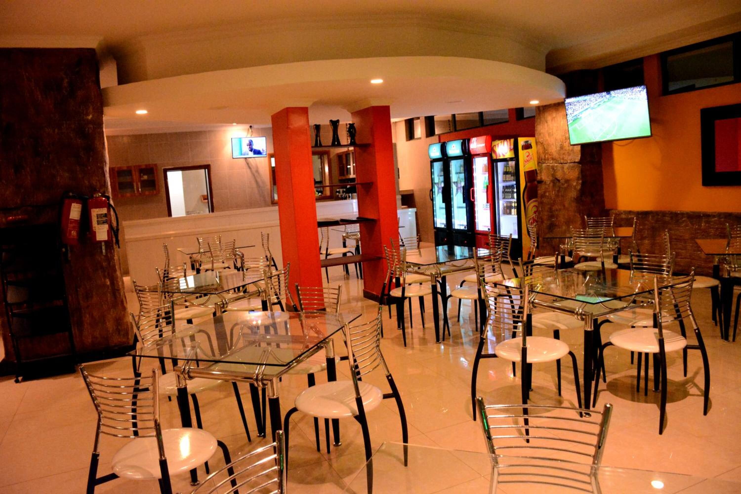 Un restaurante con mesas y sillas de vidrio, pilares rojos y un televisor montado en la pared.