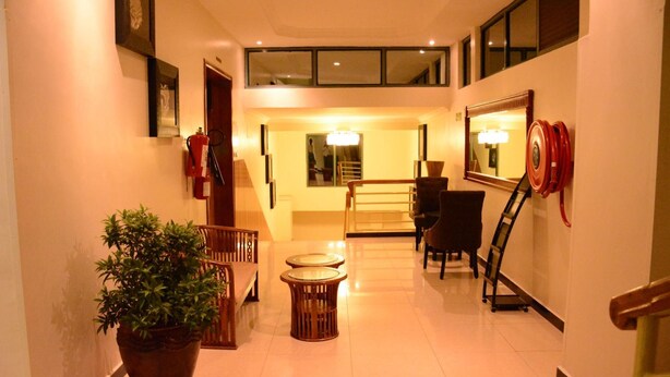 A hotel hallway with a potted plant, two round tables, a chair, a fire extinguisher, a mirror, and a staircase leading to an upper level. - La Posh Hotel (Kigali)