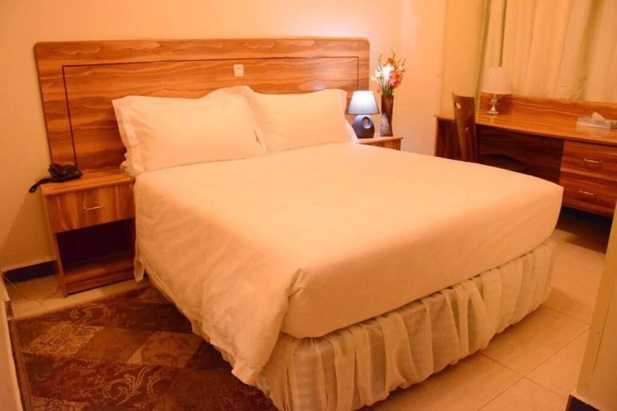 A neatly made bed with a wooden headboard, a bedside table with a lamp, and a small desk with a chair.