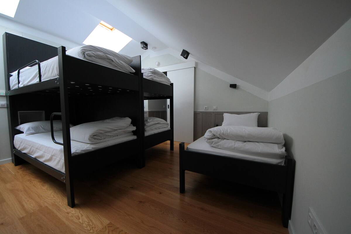 Un dormitorio con dos literas, una cama individual, suelo de madera y un tragaluz.