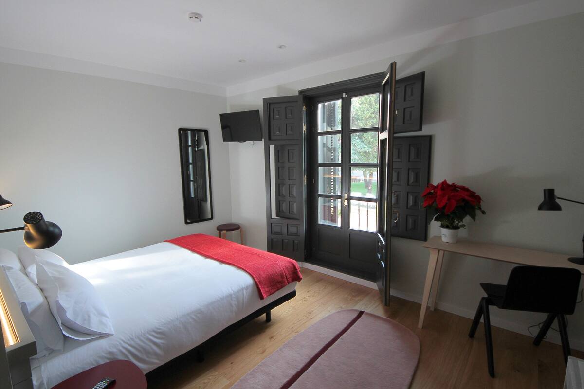 Un dormitorio con cama, escritorio, silla, televisor y puerta.