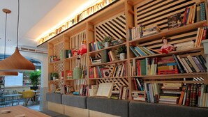 A cozy library with bookshelves, seating areas, and a wooden table. - Complutum Hostel (Alcala de Henares)