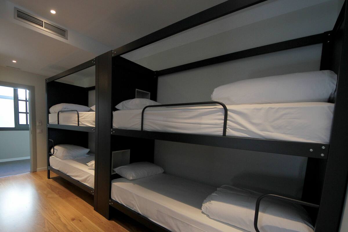 Habitación con literas de tres niveles, piso de madera y ventana que proporciona luz natural.