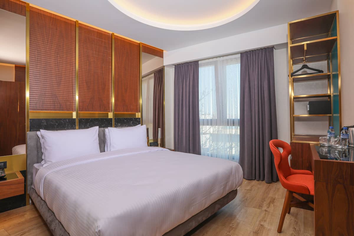 Une chambre d’hôtel avec un grand lit, un bureau avec une chaise, une armoire et un balcon avec des rideaux.