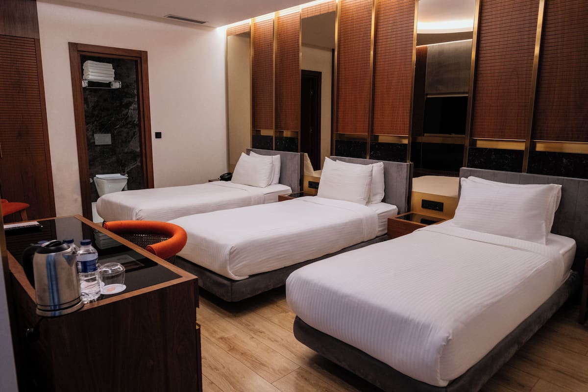 Une chambre d’hôtel avec deux lits, un bureau avec une bouilloire et des bouteilles d’eau, un miroir et un plancher en bois.