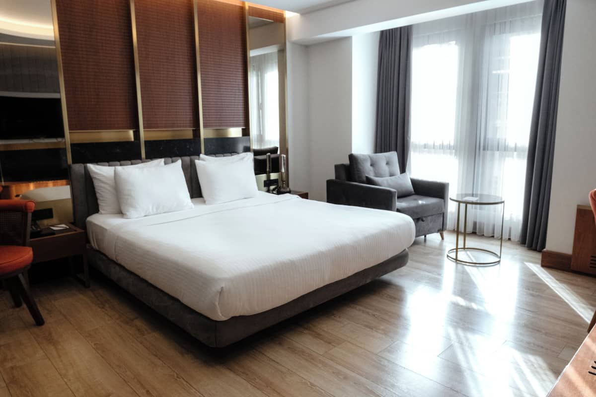 Une chambre d’hôtel avec un grand lit, un bureau, une chaise, une table ronde et une grande fenêtre avec des rideaux.