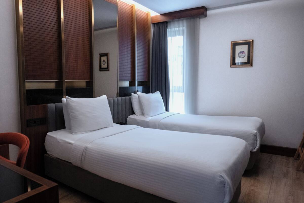 Une chambre d’hôtel avec deux lits, un bureau, une chaise, un miroir et un tableau encadré au mur.