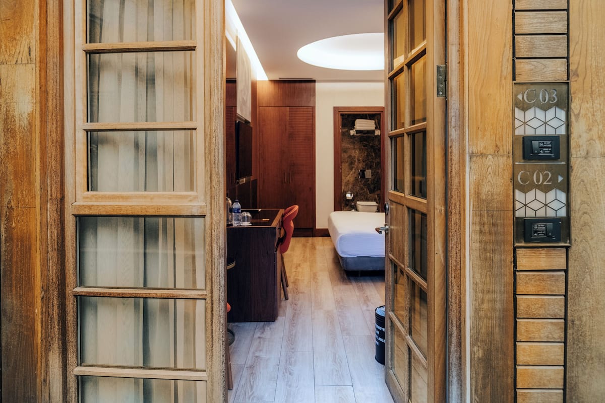 Un couloir étroit avec des portes en bois, un petit bureau avec une chaise, un lit et une salle de bain avec une douche.