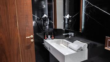 Une salle de bain moderne avec un lavabo blanc, des murs en marbre noir et un grand miroir.