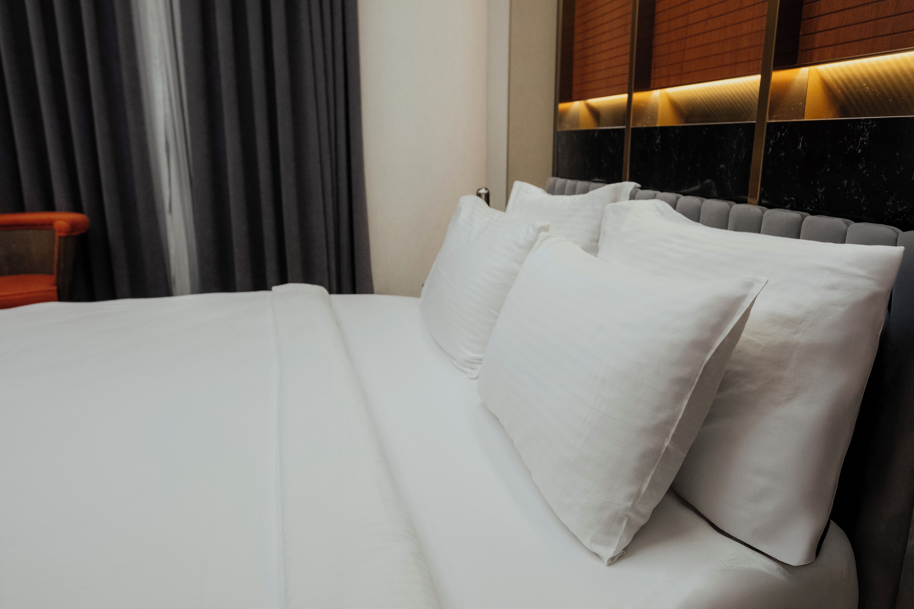 A hotel room with a neatly made bed, a chair, and a window with blinds.