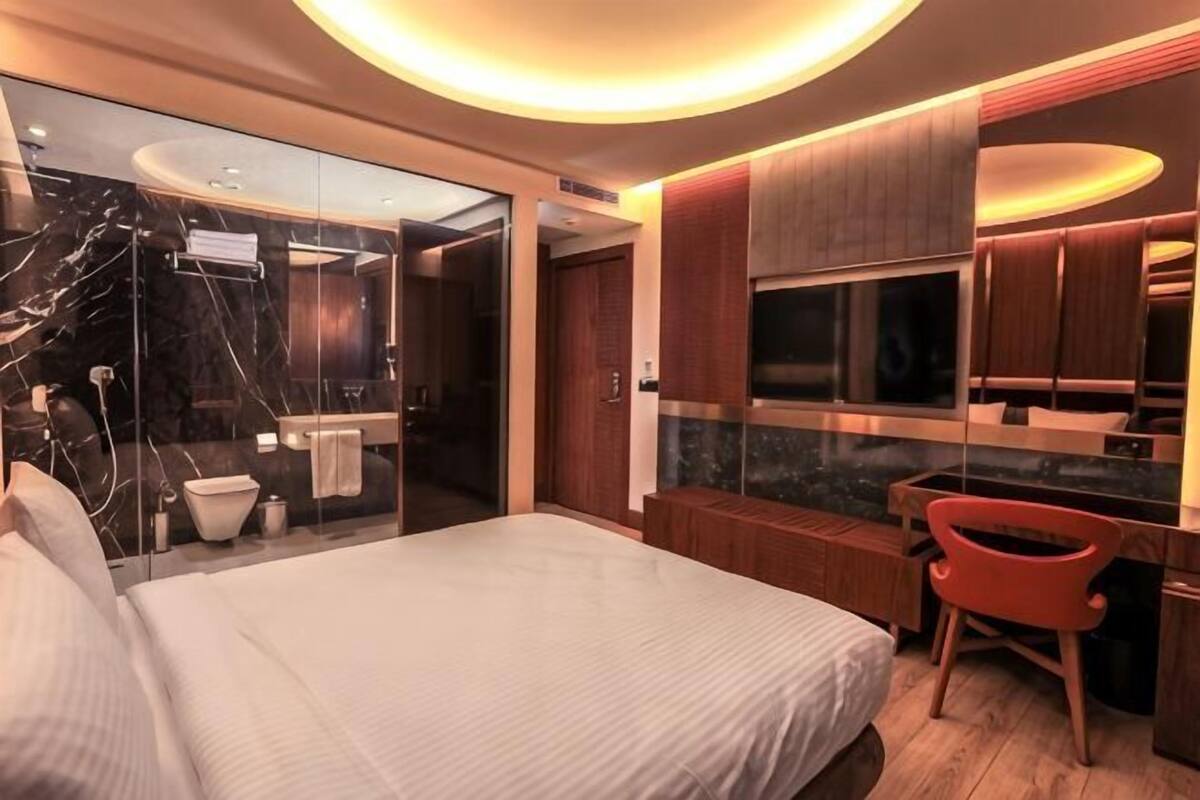 Une chambre d’hôtel moderne dotée d’un grand lit, d’une douche à parois de verre, d’une coiffeuse en bois et d’un téléviseur fixé au mur.