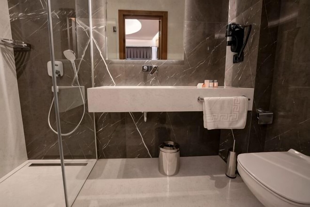 A modern bathroom with a glass shower enclosure, a marble-tiled wall, a white sink, and a toilet.