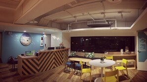 A modern interior with a wooden reception desk, a round table with yellow chairs, and a large window. - Paper Plane Hostel (Kaohsiung)