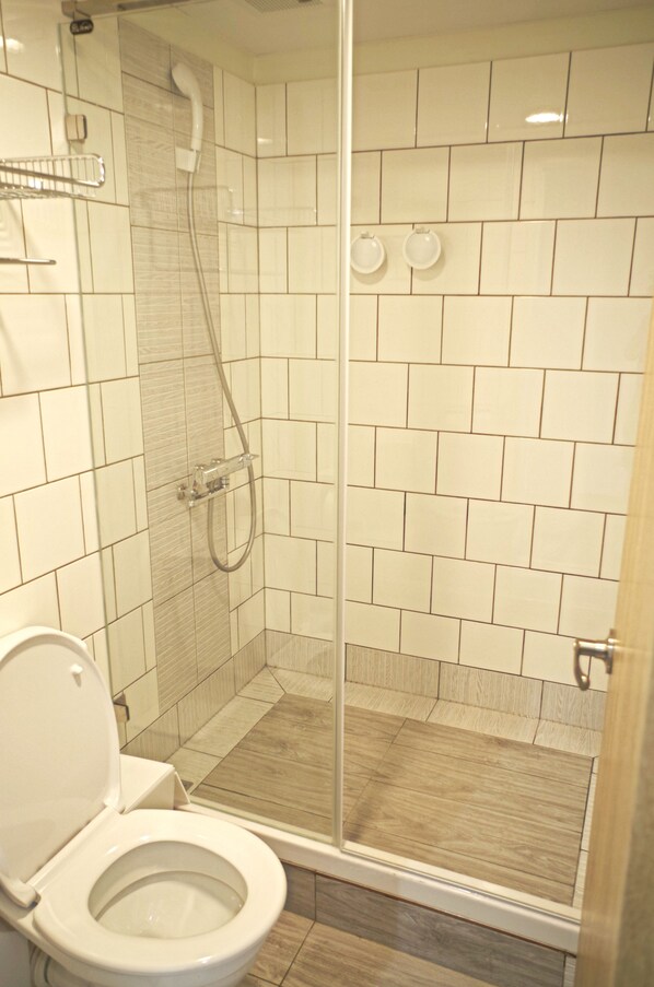 A bathroom with a toilet, a shower with a glass door, and tiled walls.