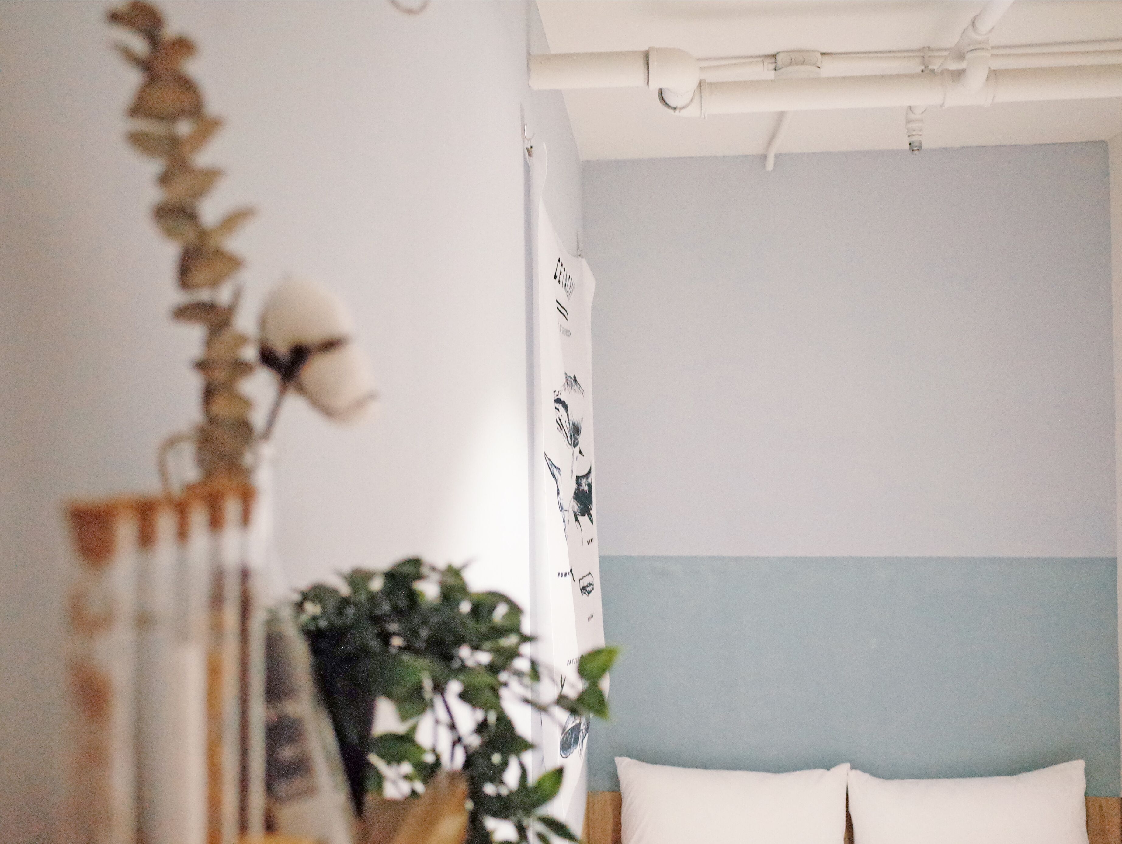 A bedroom with a bed, a wall with a light blue panel, and a white ceiling with exposed pipes.