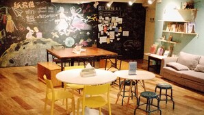 A cozy cafe with wooden flooring, yellow chairs, a round table, and a mural on the wall. - Paper Plane Hostel (Kaohsiung)