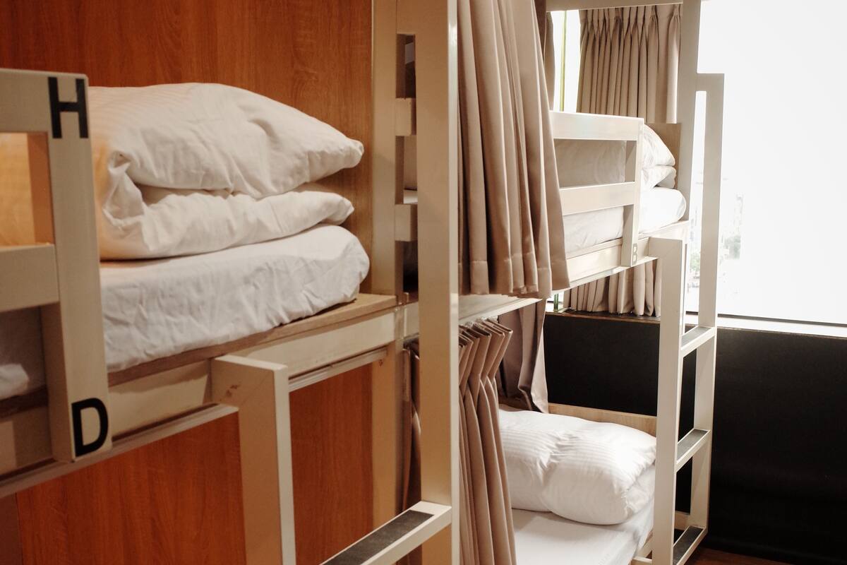 A dormitory-style room with bunk beds, wooden walls, and a window with curtains.