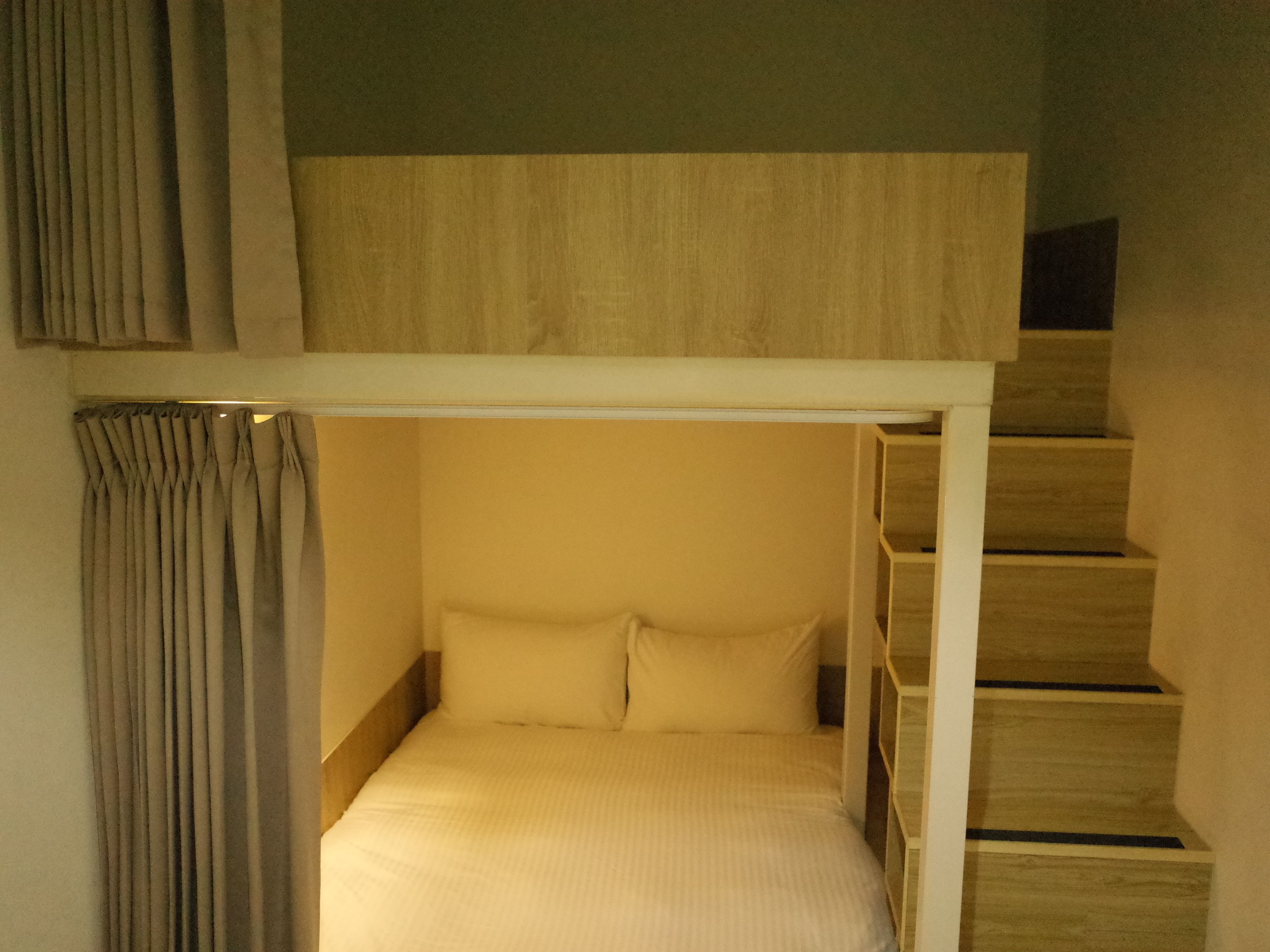 A bunk bed with a white frame, a headboard, and a mattress. There is a curtain on the left side.