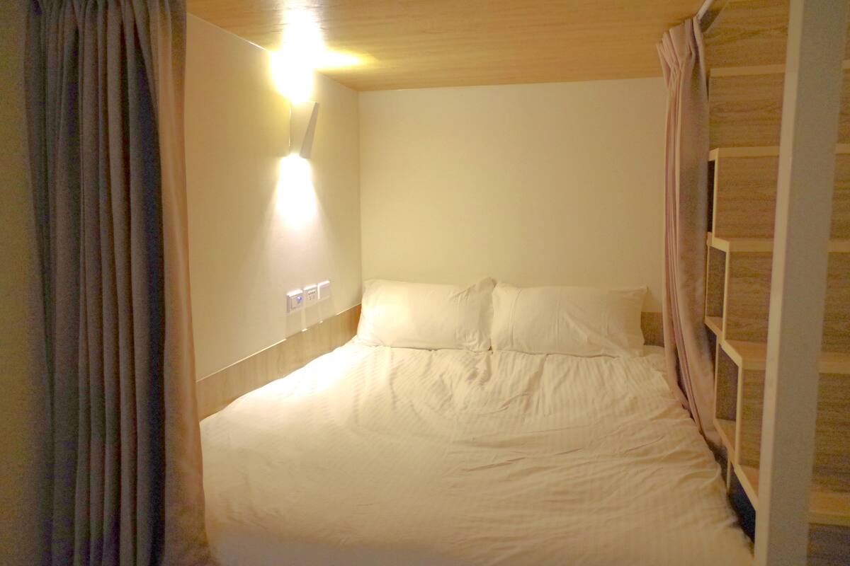 A single bed with white bedding in a room with wooden walls and a light fixture above the bed.