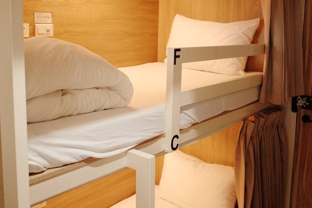 A bunk bed with white bedding, wooden walls, and a hanging coat rack.