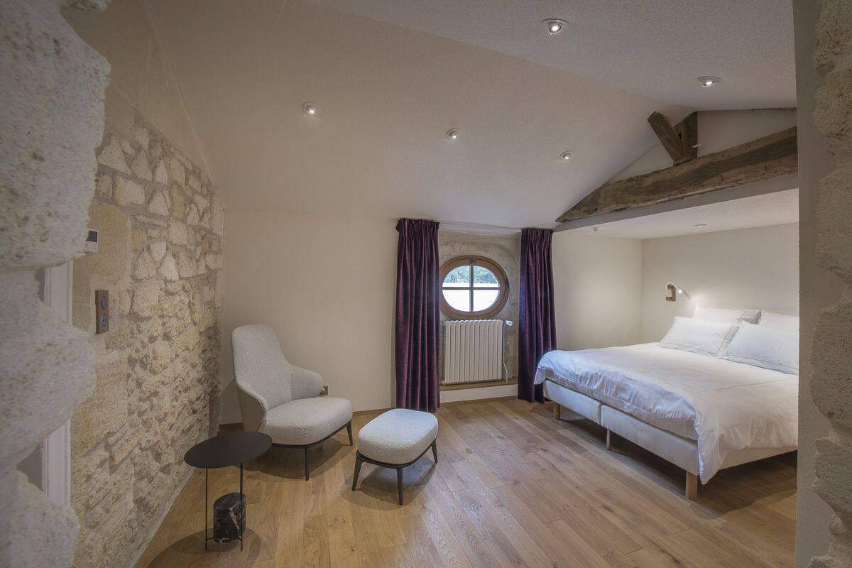 Une chambre avec un mur en pierre, un lit, une chaise et une petite table.