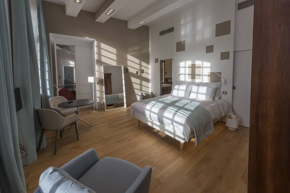Une chambre d’hôtel moderne avec un grand lit, un bureau et une chaise. On peut apercevoir la salle de bain à travers une porte ouverte.