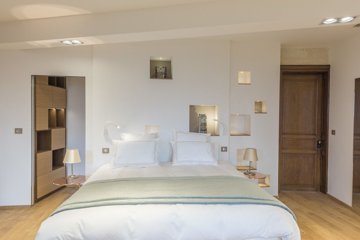 A modern hotel room with a large bed, bedside tables, a wardrobe, and a wooden door.