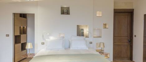 A modern hotel room with a large bed, bedside tables, a wardrobe, and a wooden door.
