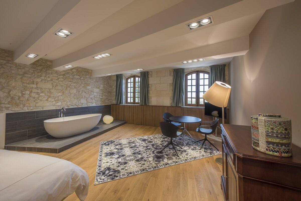 Une salle de bain moderne avec une baignoire sur pieds, une table ronde avec des chaises et une grande fenêtre avec des rideaux.