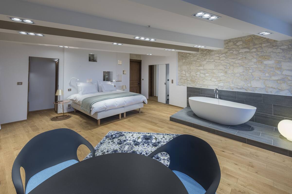 Une chambre moderne avec un grand lit, un coin salon avec une table et une salle de bain dotée d’une grande baignoire.
