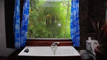 A bathroom with a bathtub, a window with curtains, and a toilet.