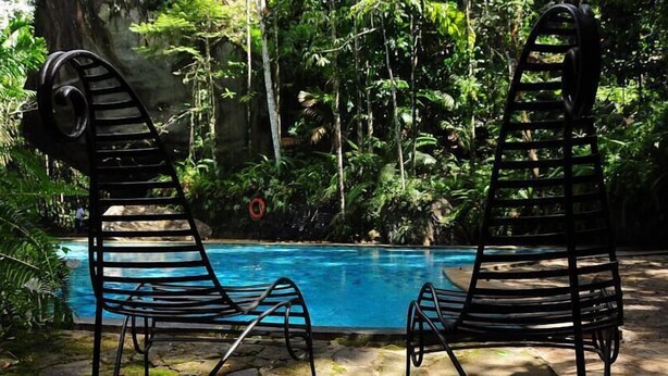 Two black lounge chairs by a pool with a tropical backdrop. - Boulder Garden Hotel (Kalawana)