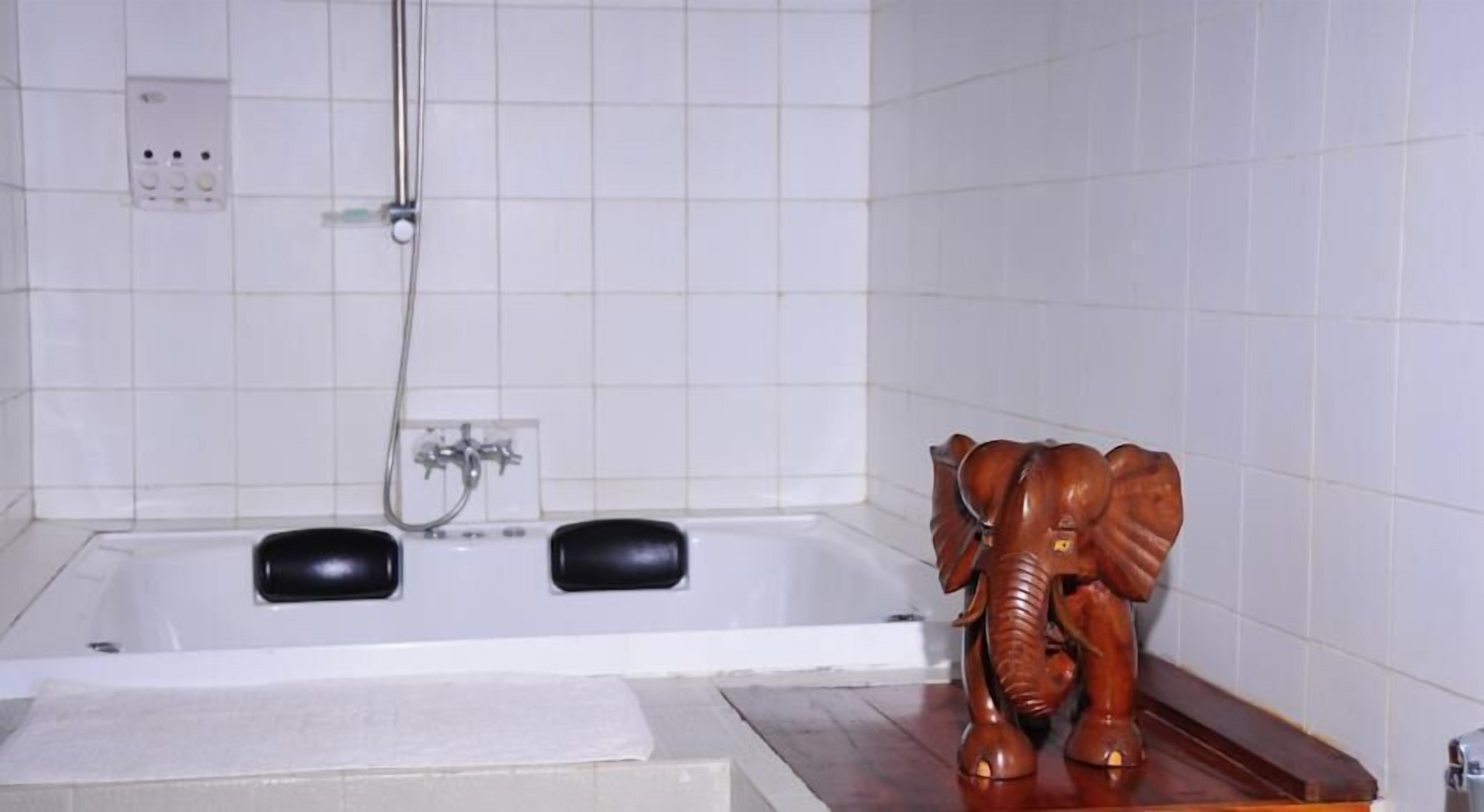Een badkamer met een bad, een houten olifant decoratie en een betegelde muur.