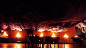 An underground restaurant with tables and chairs, illuminated by candlelight. - Boulder Garden Hotel (Kalawana)