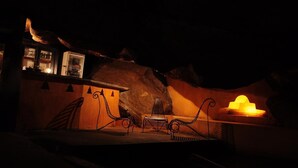A dimly lit room with a large rock formation, a small table with a chair, and a wall-mounted shelf with various items. - Boulder Garden Hotel (Kalawana)