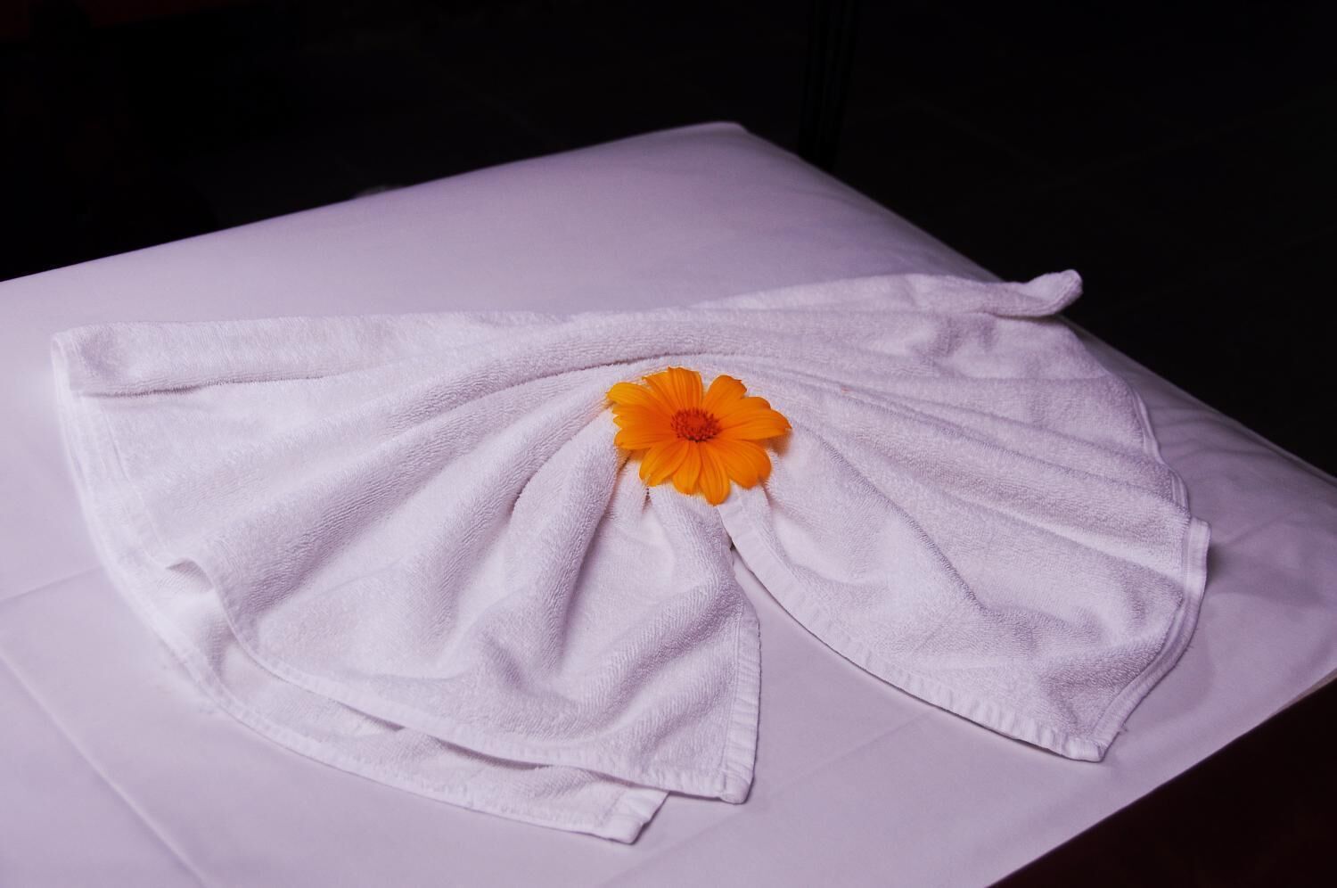 A white towel with a flower on a table.