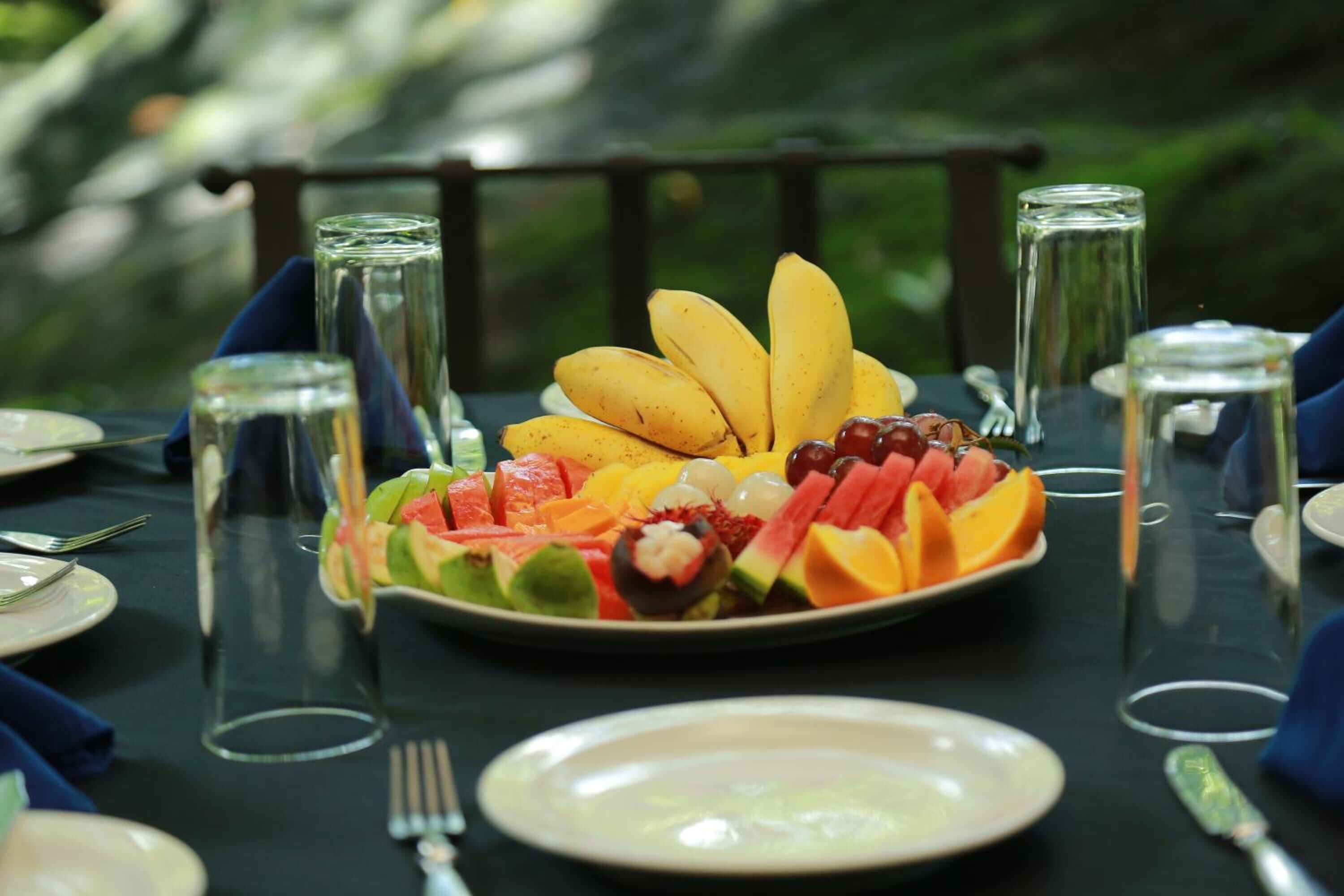 A table set for a meal with a fruit platter, clear glasses, and cutlery.