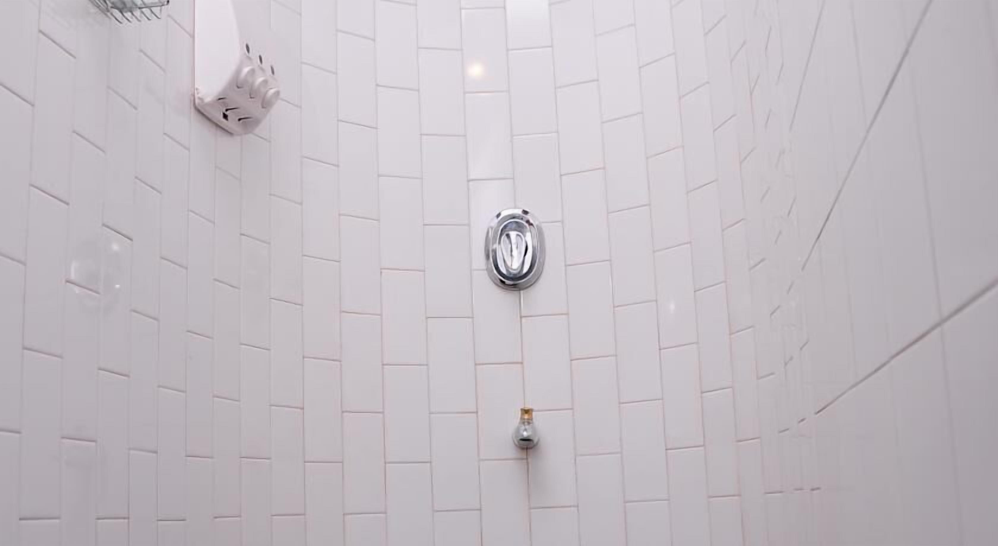 Un baño con paredes de azulejos blancos y zona de ducha.